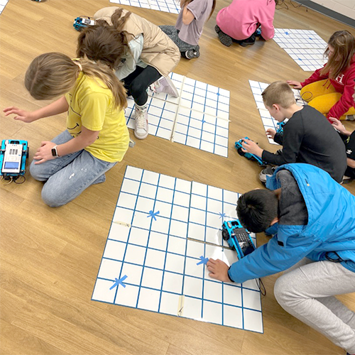 Students using a TI graphing calculator and TI-Innovator™ Rover to graph on a coordinate plane using paper. 