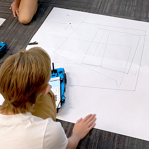 Students using a TI graphing calculator and TI-Innovator™ Rover to draw graph ordered pairs using a sheet of poster board.